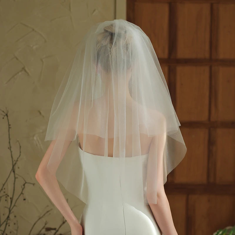 Person wearing a white wedding dress with a veil in front of a textured wall.
