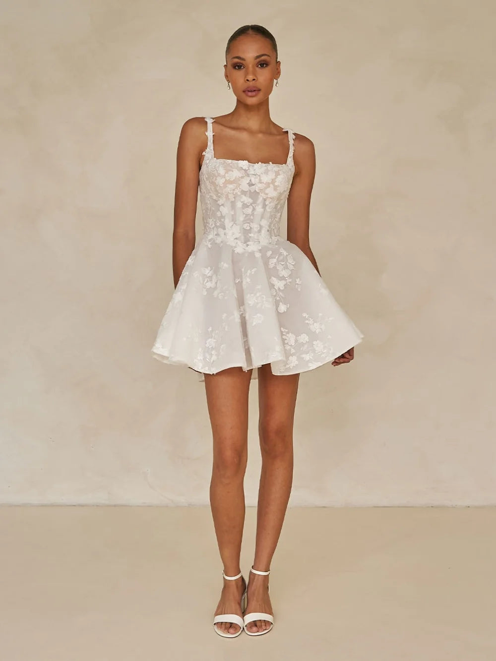 Woman wearing a white floral dress against a beige background