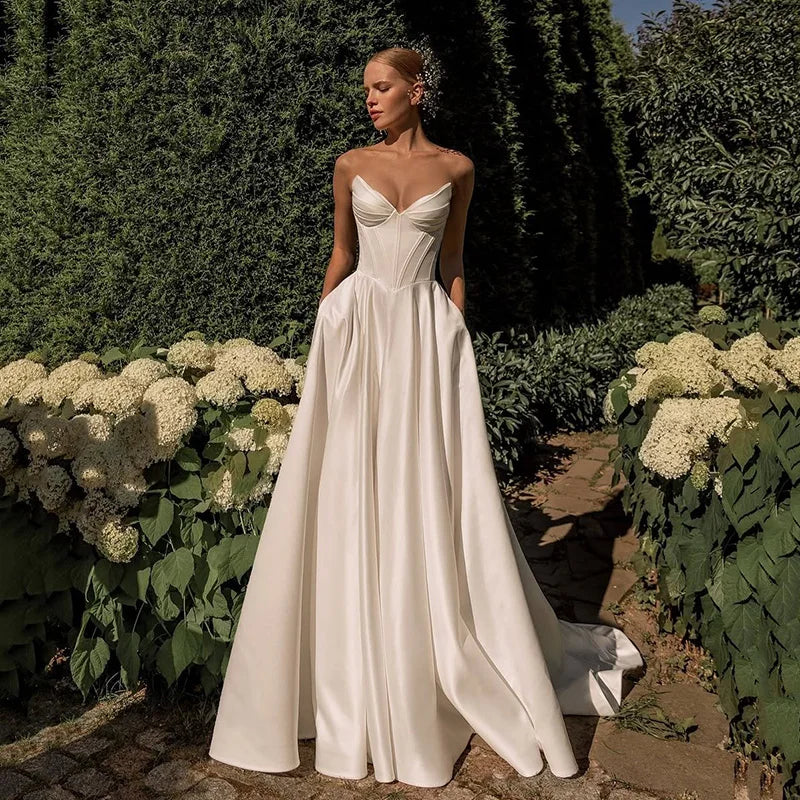 Woman in a white wedding dress standing in a garden with greenery and flowers.
