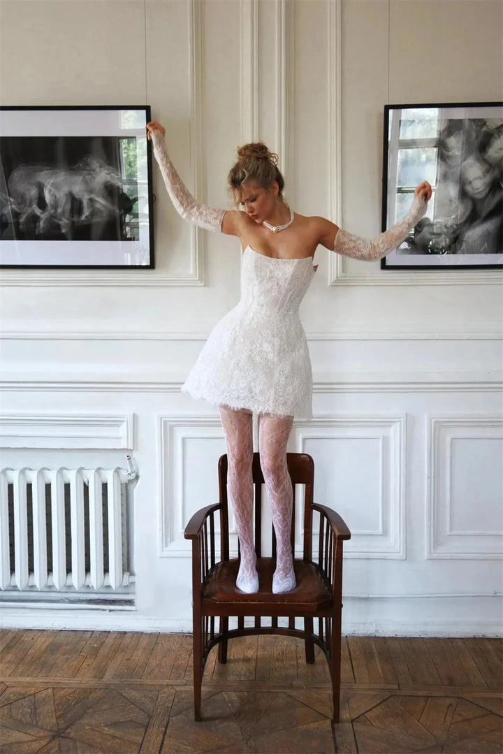 Woman in a white dress standing on a chair in a room with framed pictures on the wall.