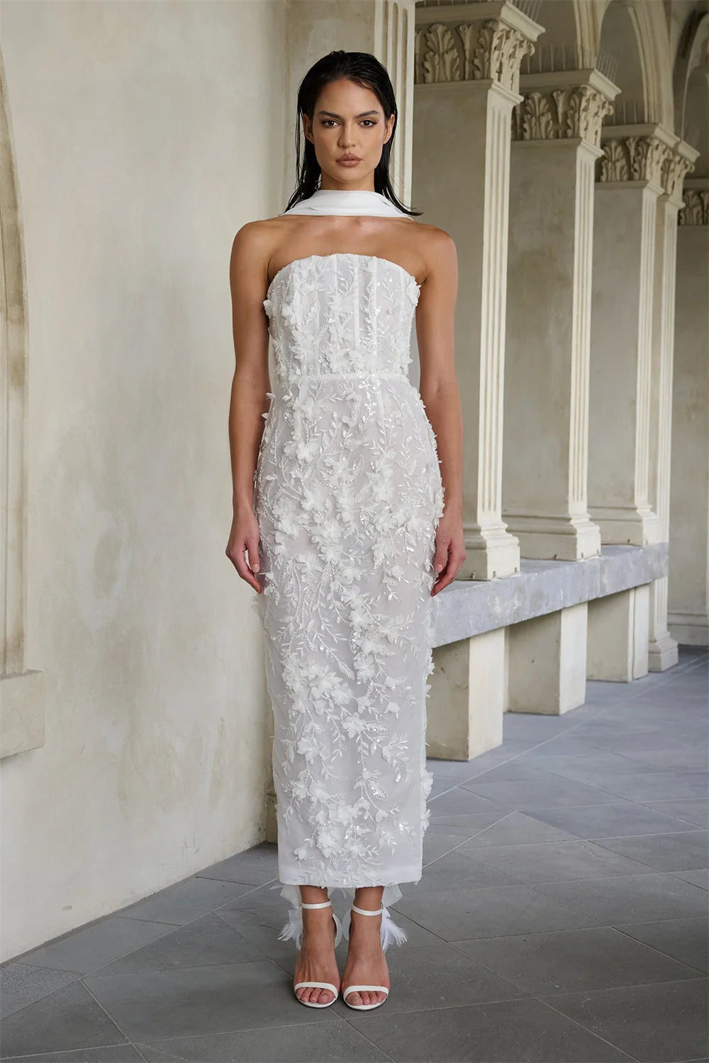 Woman wearing a white strapless dress with floral details in an elegant hallway.