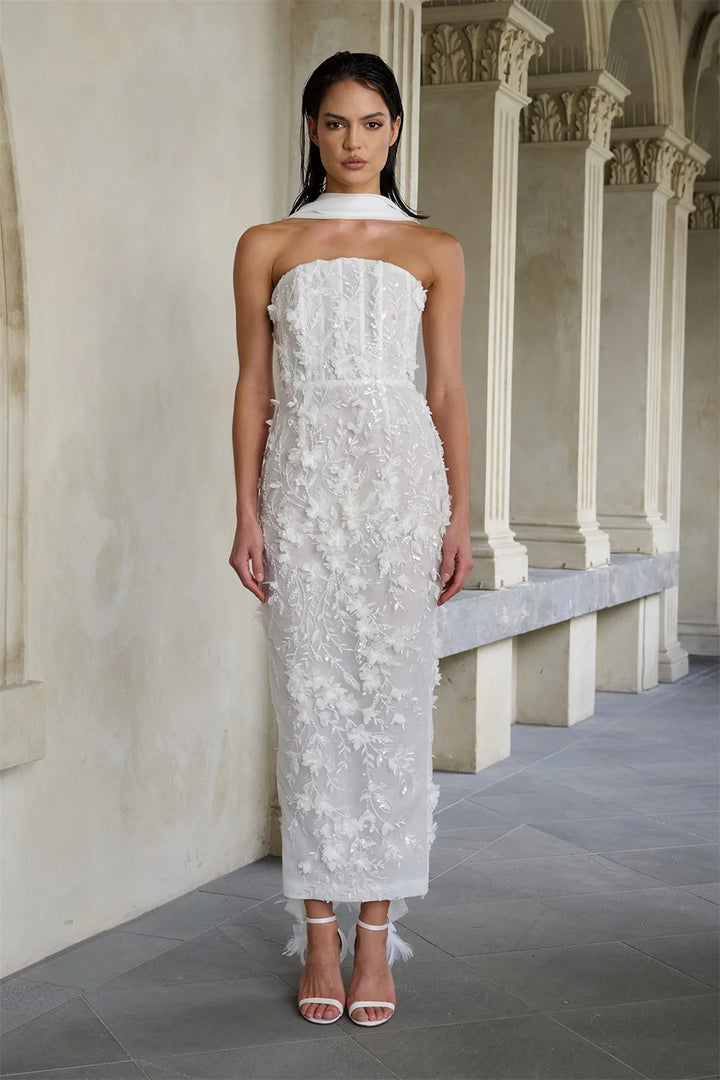 Woman wearing a white strapless dress with floral details in an elegant hallway.
