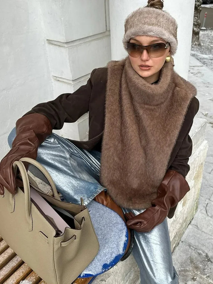 Woman in winter clothing with a fur scarf, sunglasses, and a beige handbag.