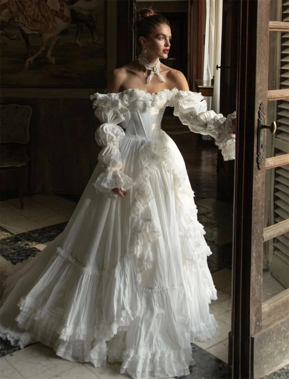 Woman in a white, off-shoulder, ruffled gown standing in a room with wooden shutters.