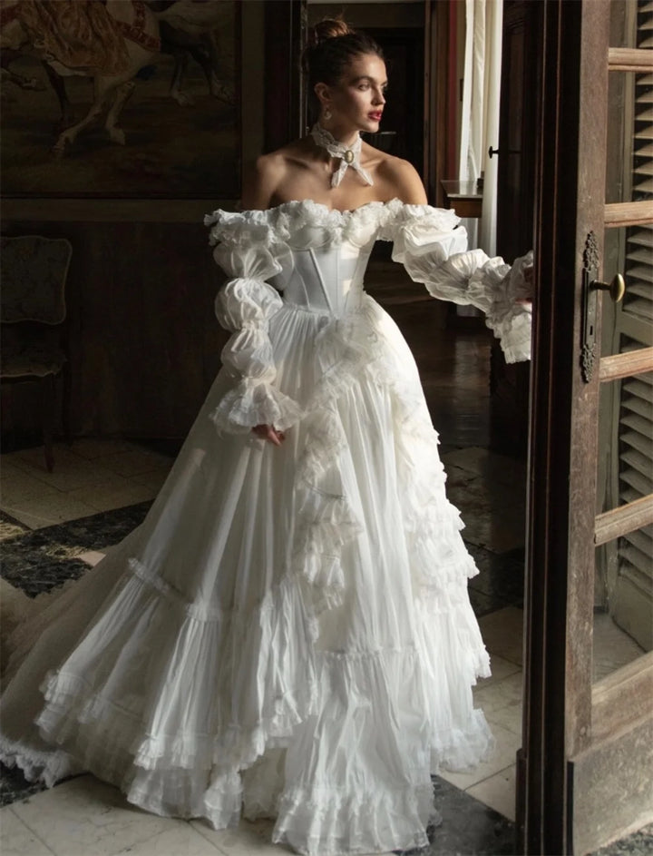 Woman in a white, off-shoulder, ruffled gown standing in a room with wooden shutters.