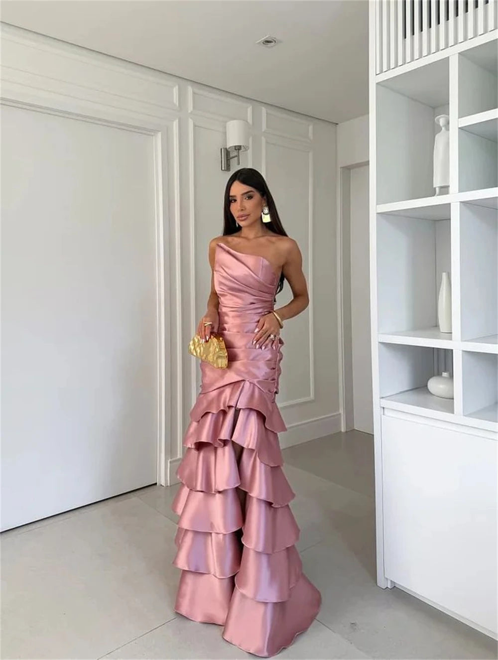 Woman in a pink one-shoulder gown standing in a modern interior setting.