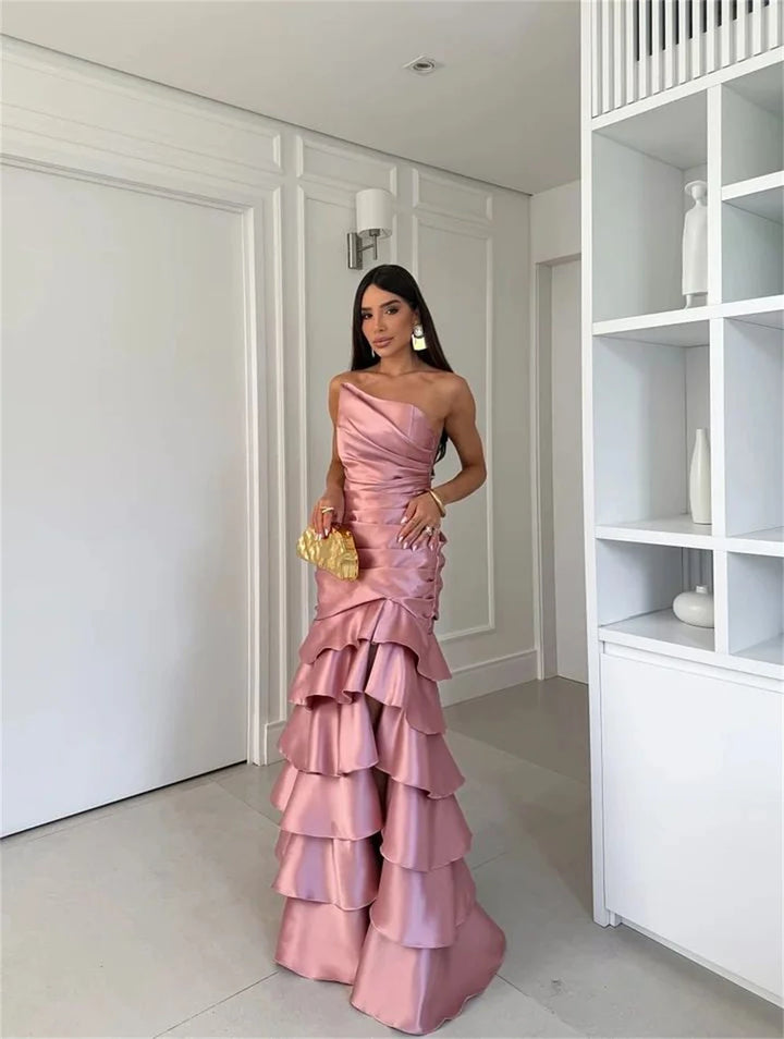 Woman in a pink one-shoulder gown standing in a modern interior setting.