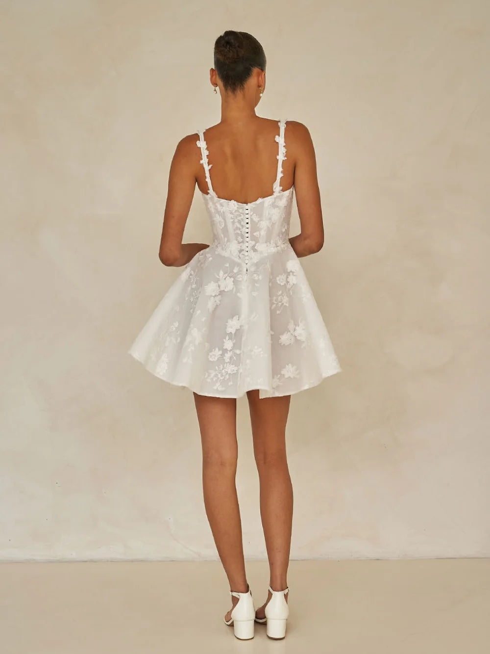Woman wearing a white floral dress against a beige background