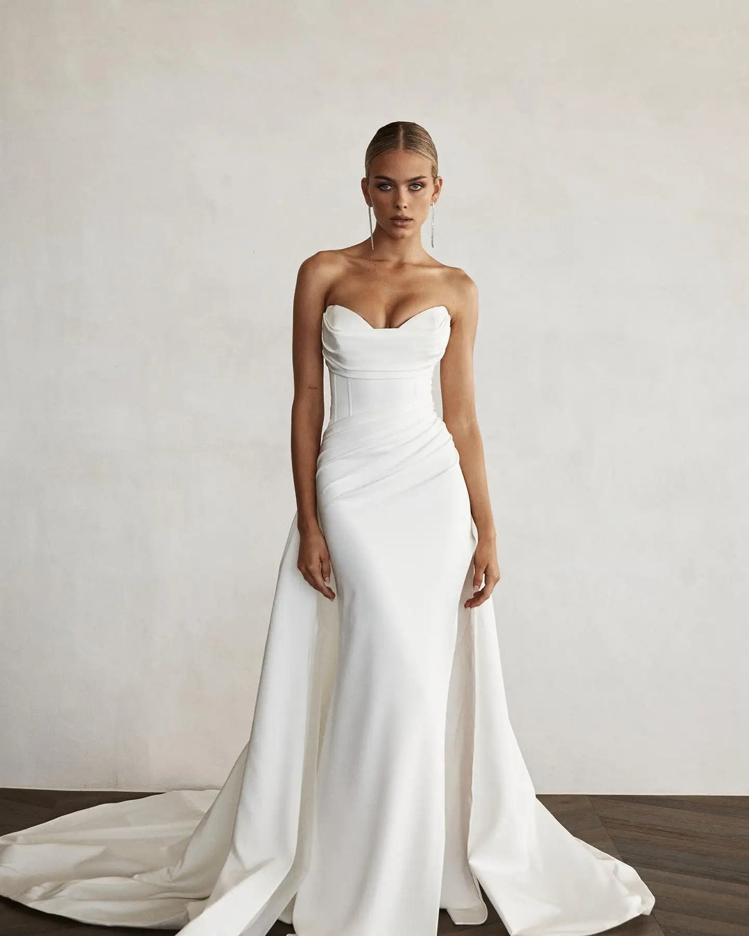 Woman wearing a white strapless wedding dress with a long train against a plain background