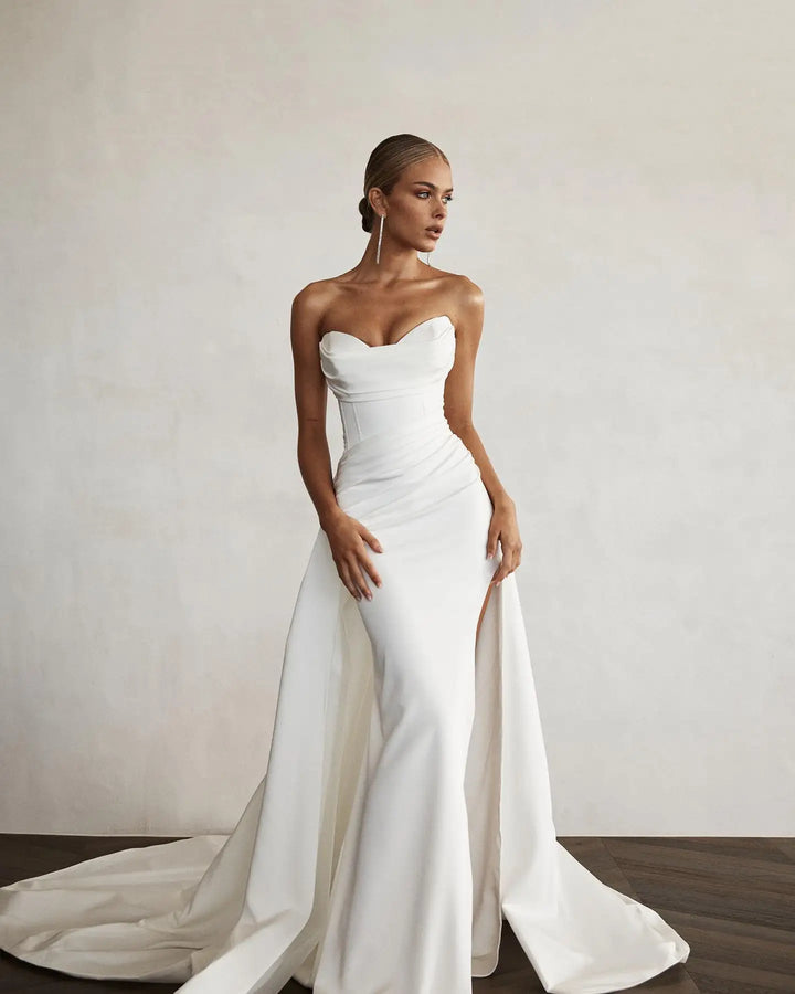Woman wearing a white strapless wedding dress with a long train against a plain background