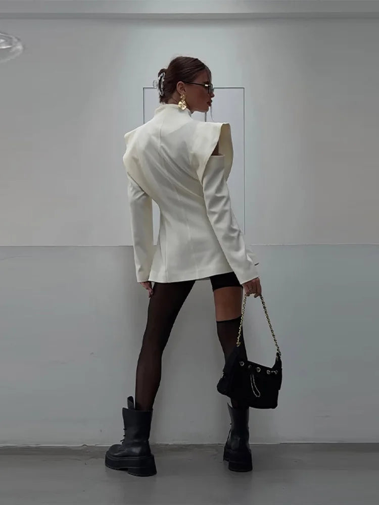 Person wearing a white blazer, black tights, and black boots against a plain background