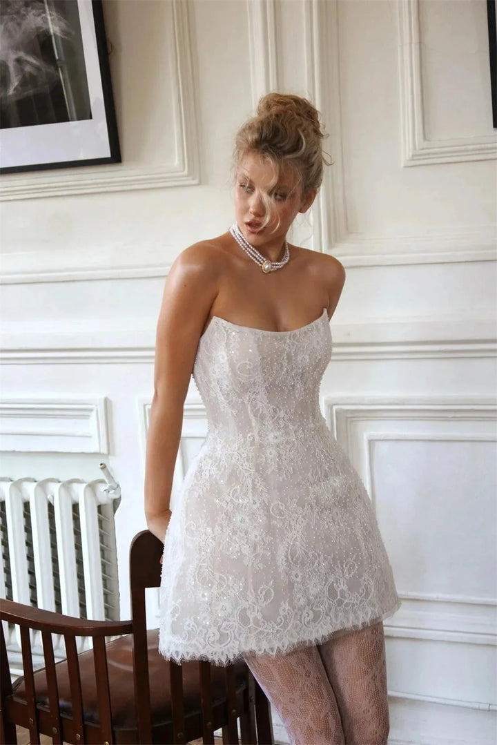 Woman in a white lace dress standing in a room with white walls and a radiator.
