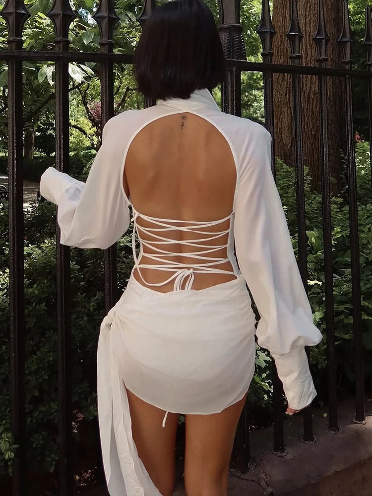 Person wearing a white outfit with an open back design, standing in front of a black metal fence.