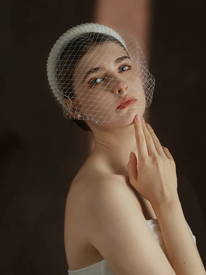 Woman wearing a white headband with a mesh veil against a dark background