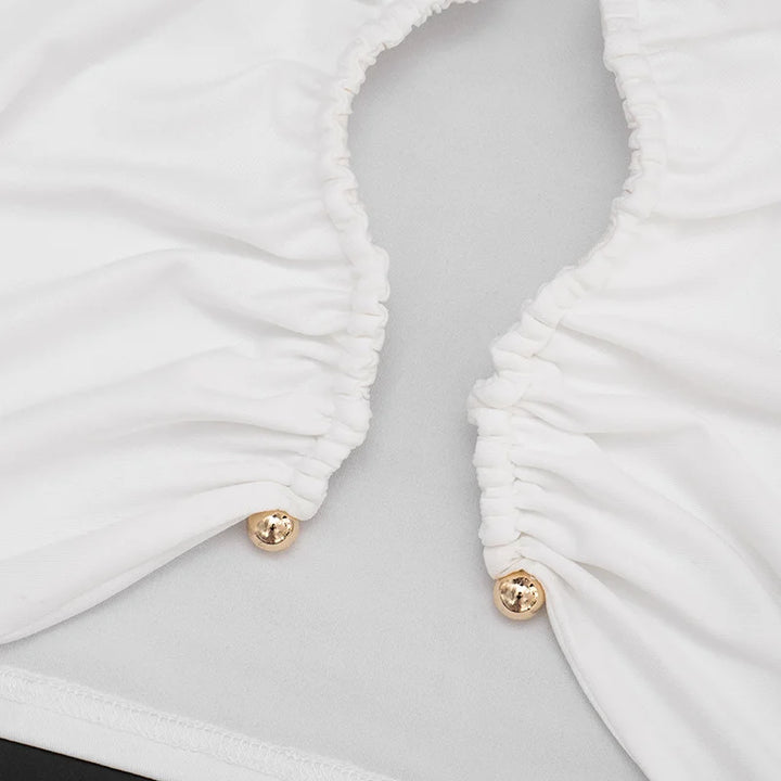 Close-up of a white ruched garment with gold buttons on a light gray background