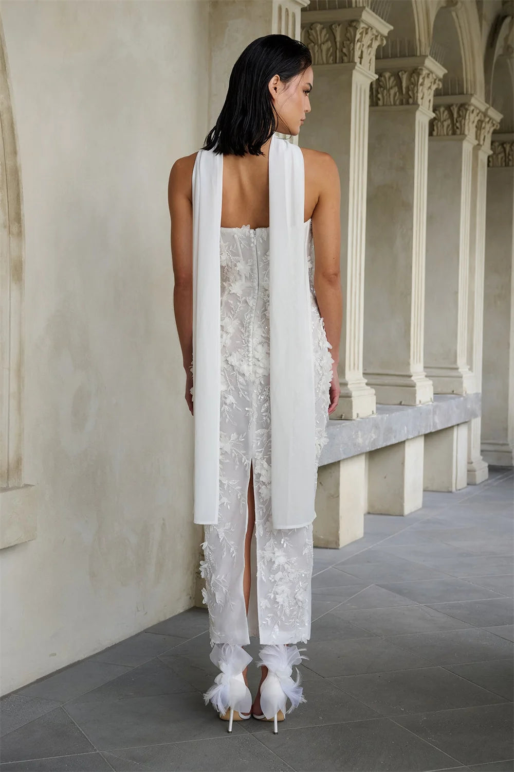 Woman in a white lace dress standing in an elegant hallway with columns.