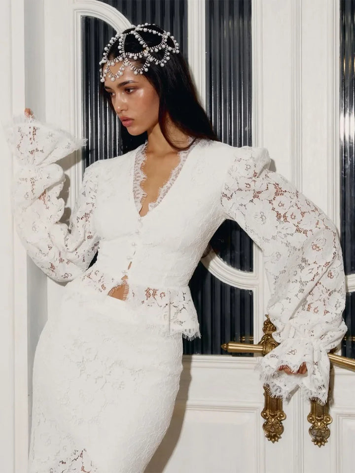 Woman wearing a white lace dress with long sleeves in front of a decorative door.