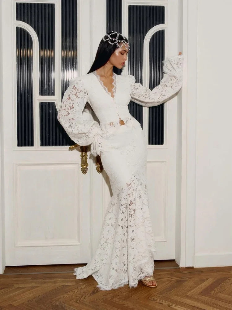Woman in a white lace dress sitting on a chair with a decorative headpiece.