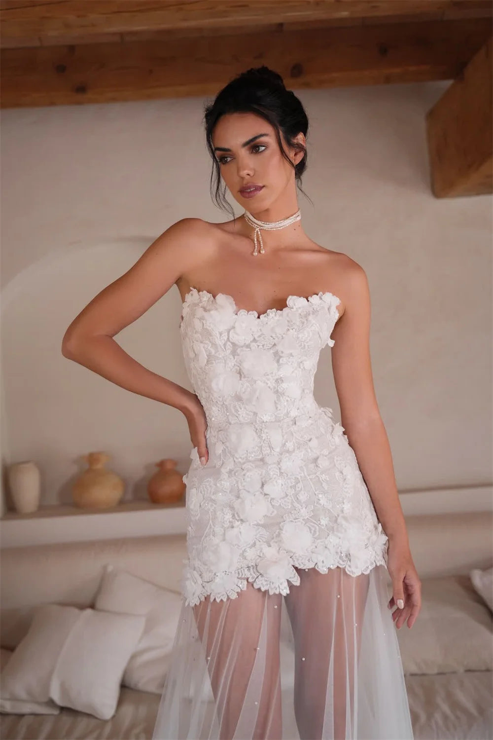 Woman wearing a white strapless dress with floral details in an indoor setting.
