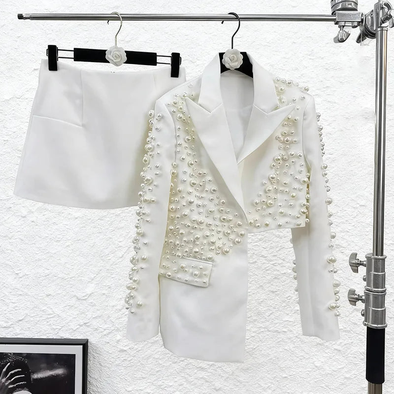 White blazer with pearl embellishments on a rack against a textured white wall.
