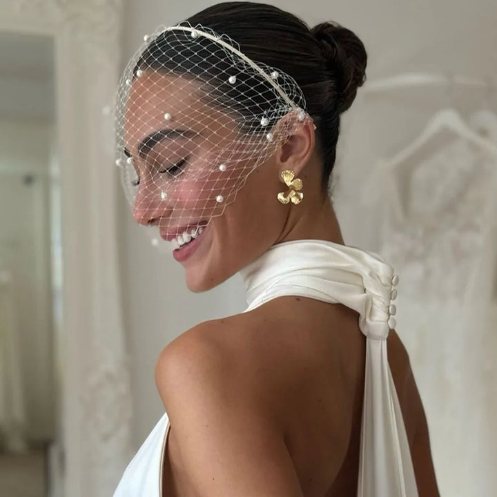 Woman wearing a birdcage veil and gold earrings in an elegant setting