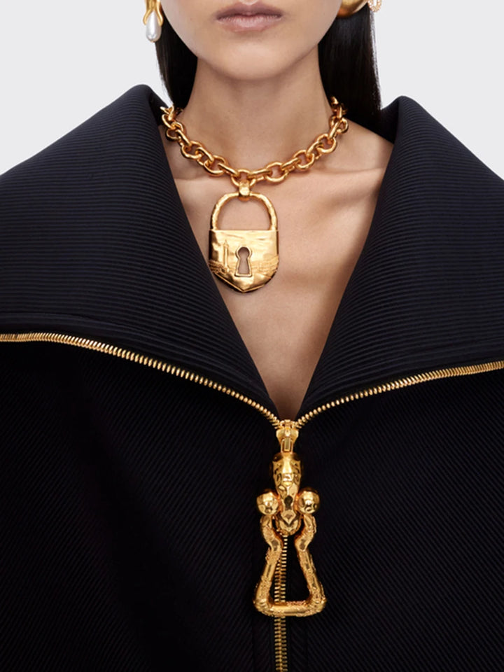 Gold necklace with a lock pendant worn by a model against a neutral background