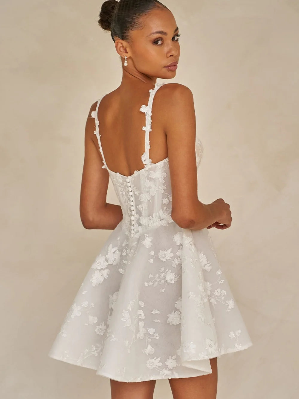 Woman wearing a white floral dress against a beige background