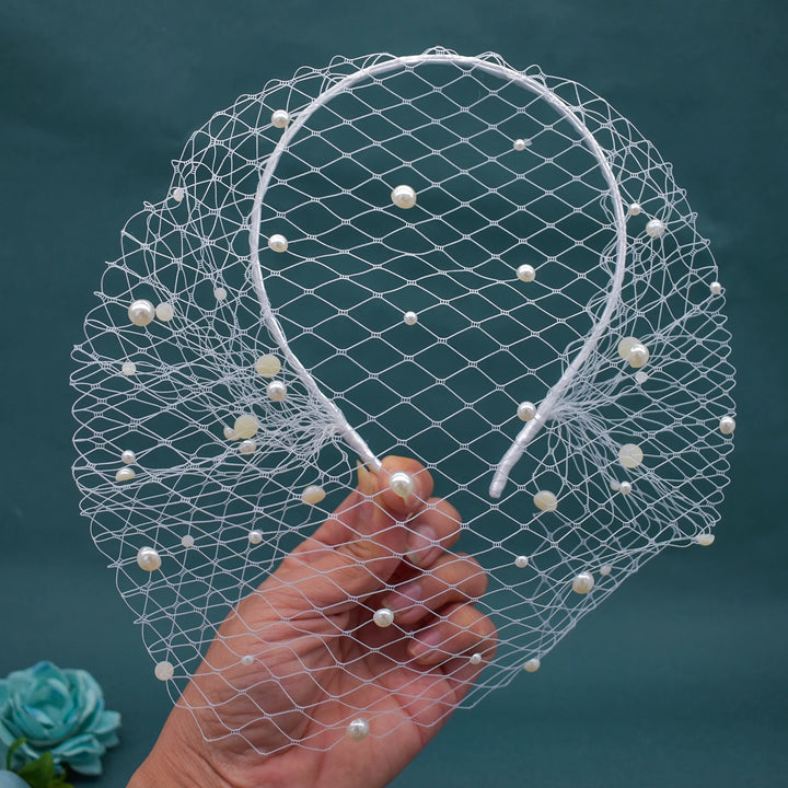 White birdcage veil with pearls held by a hand against a dark background