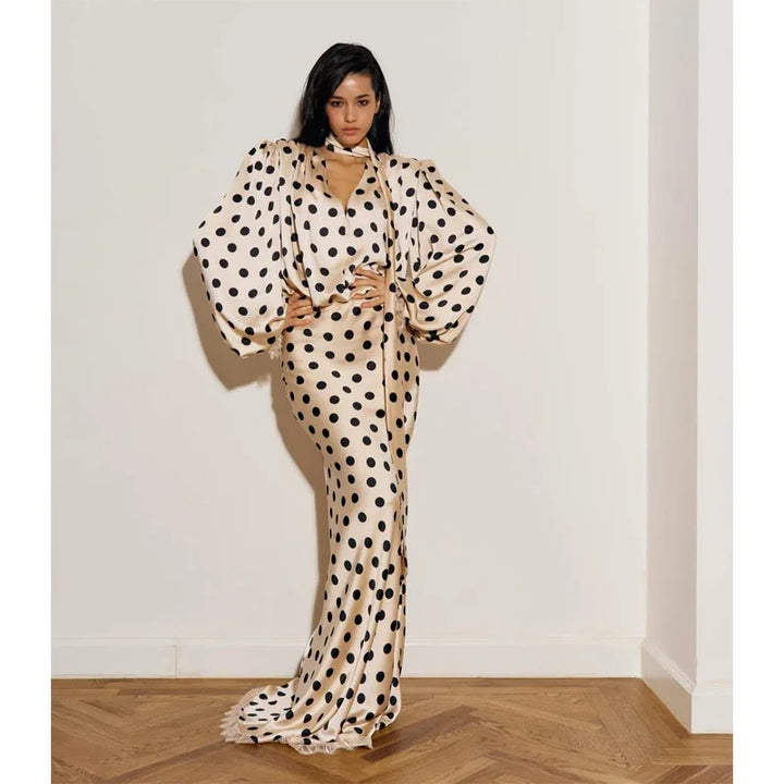 Woman wearing a polka dot dress standing against a white wall.