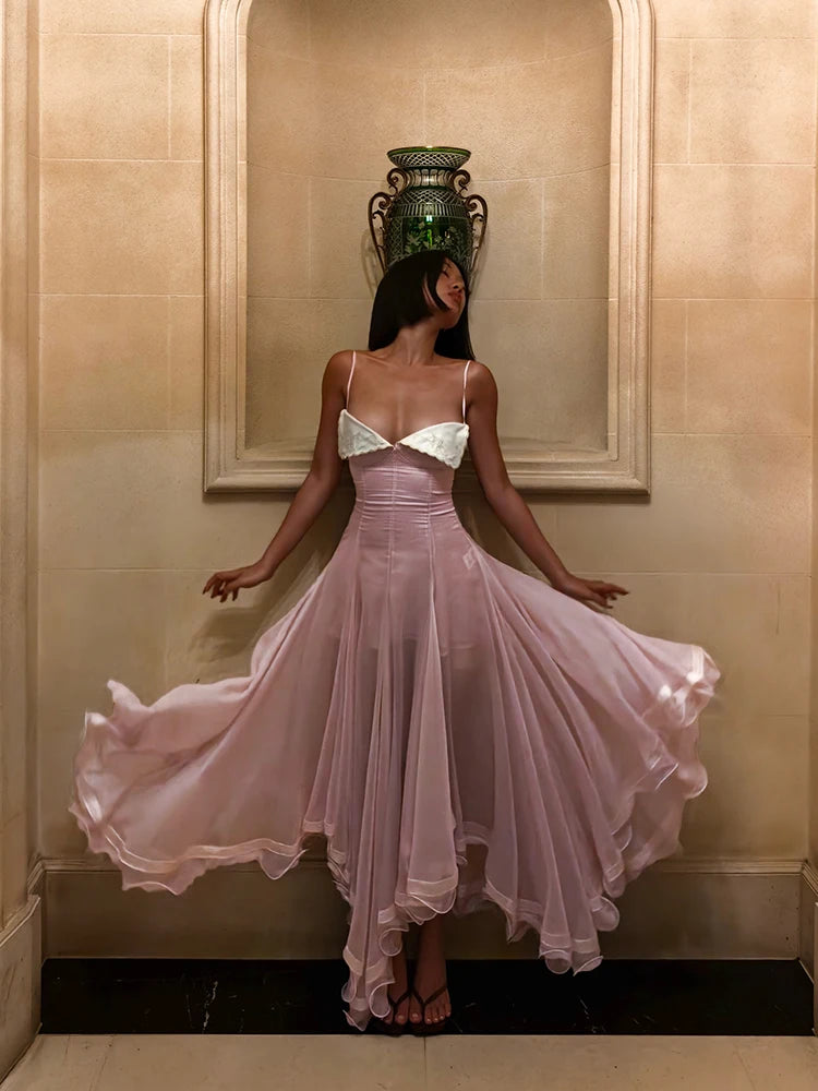 Woman in a flowing pink dress standing against a beige wall with a decorative vase.