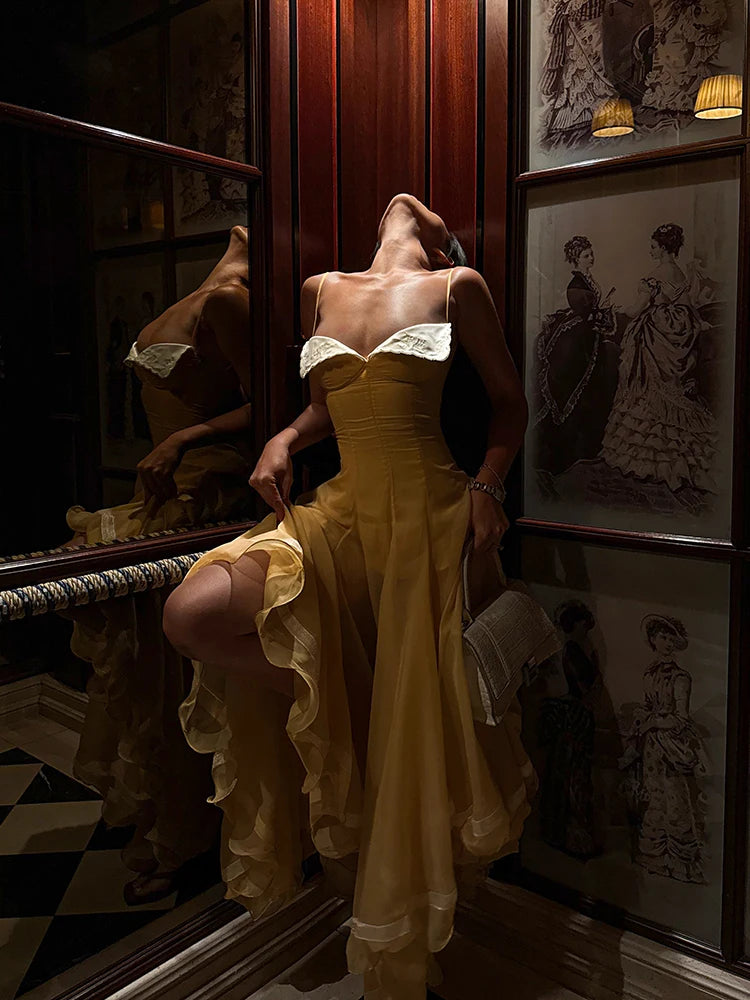 Woman in a yellow dress standing in a room with vintage decor and framed pictures.
