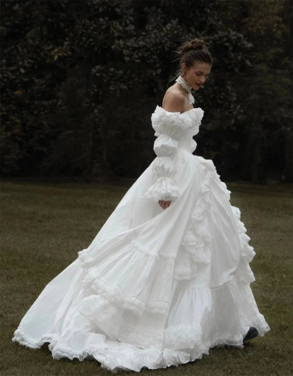 Woman in a white wedding dress standing in a grassy area with trees in the background