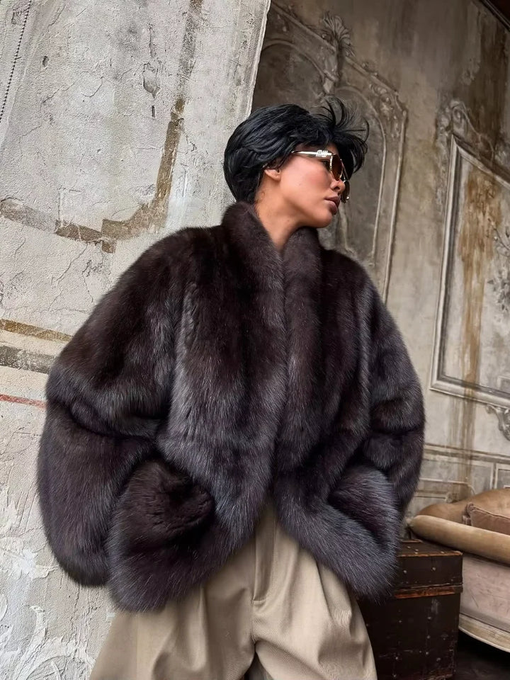 Person wearing a dark fur coat in an ornate room.