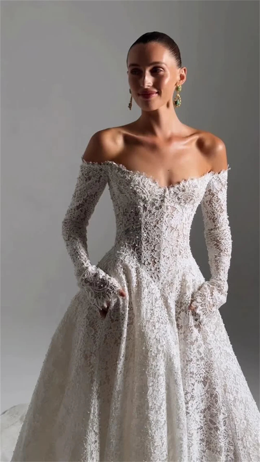 Woman wearing a white lace wedding dress with long sleeves on a gray background, brand &