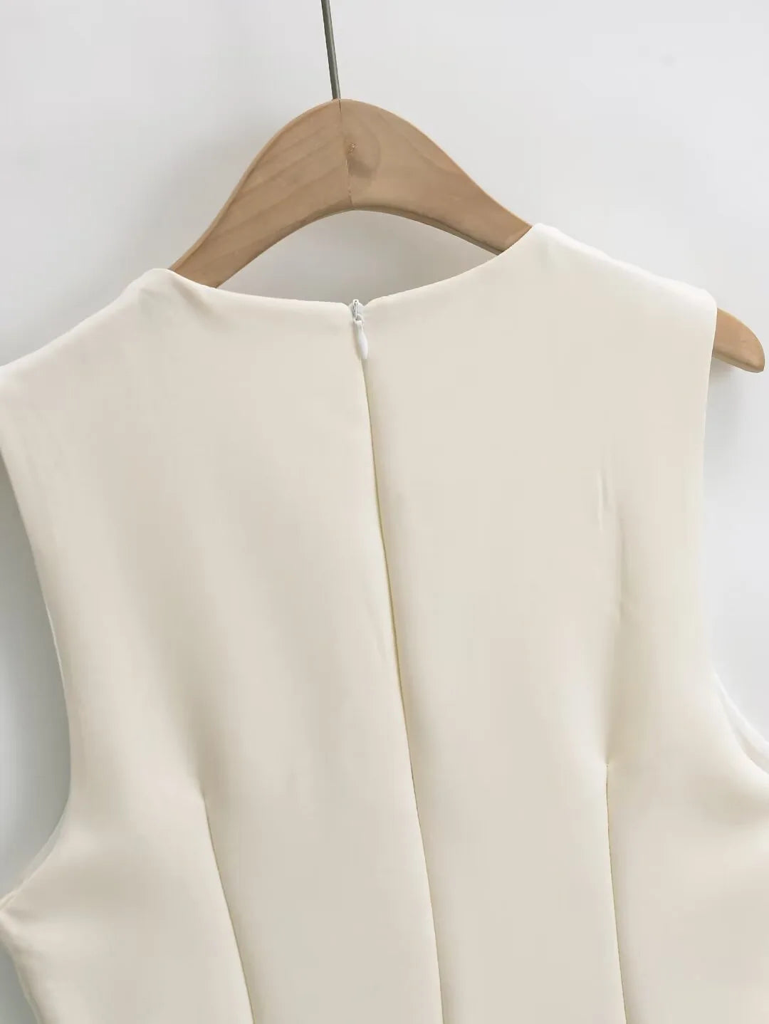 Beige sleeveless top on a wooden hanger against a white background