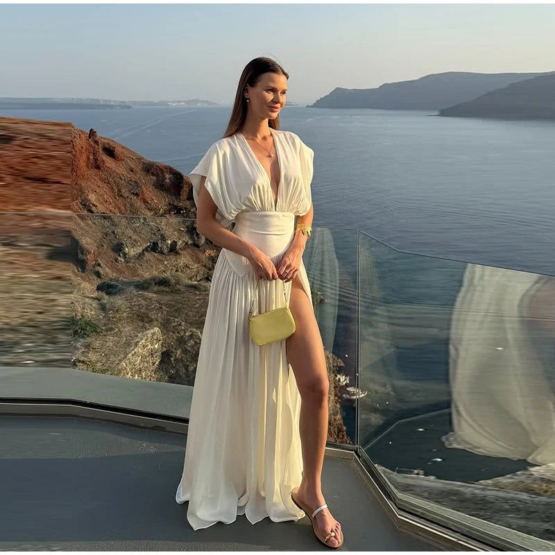 Woman in a white dress standing on a cliff overlooking the ocean.