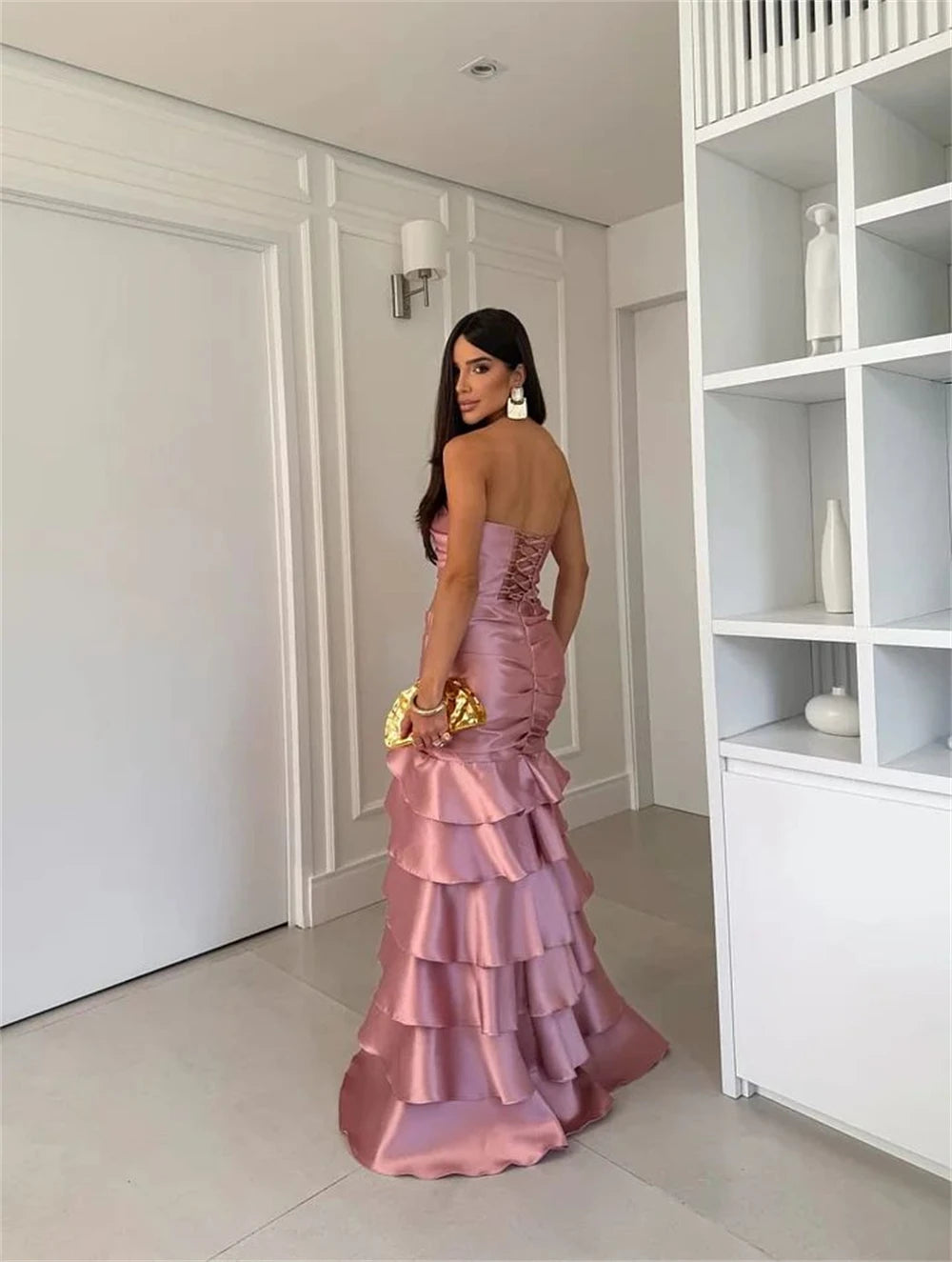 Woman in a pink ruffled dress standing in a modern interior setting.