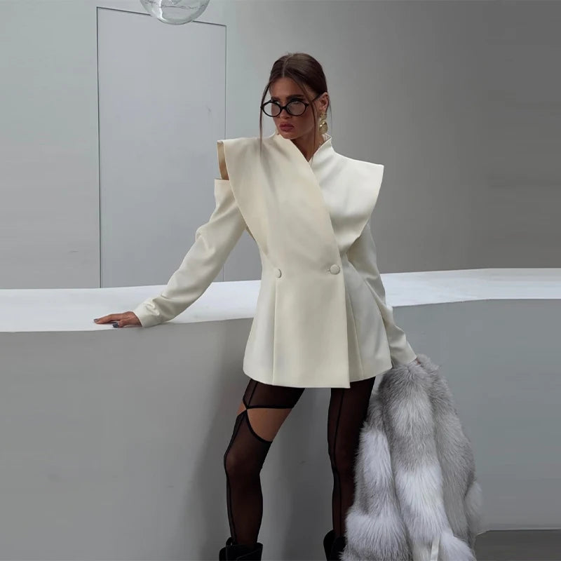 Woman in a white coat and black pants standing against a plain background