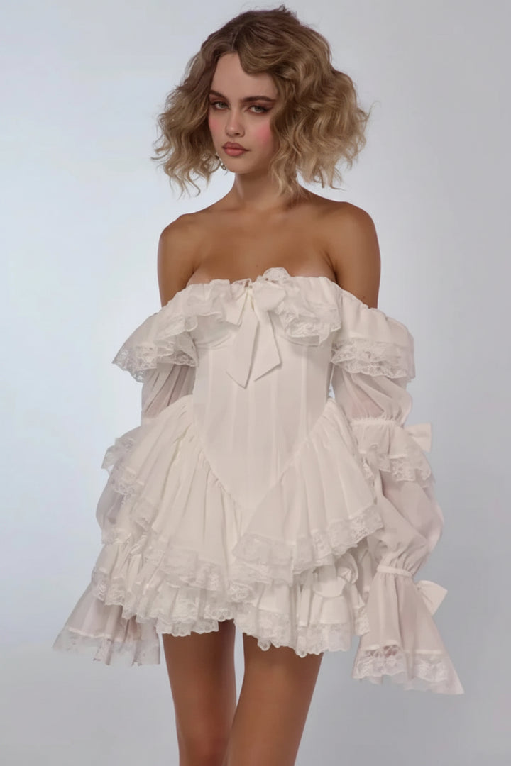 A model wearing a white off-the-shoulder ruffled mini dress with long balloon sleeves and a bow detail at the neckline, set against a plain light gray studio background. The brand name &