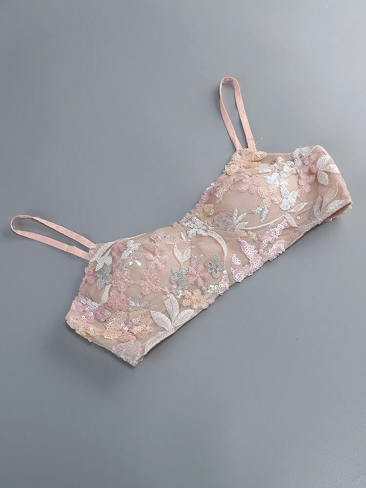 Delicate pink lace bralette with floral embroidery on a gray background