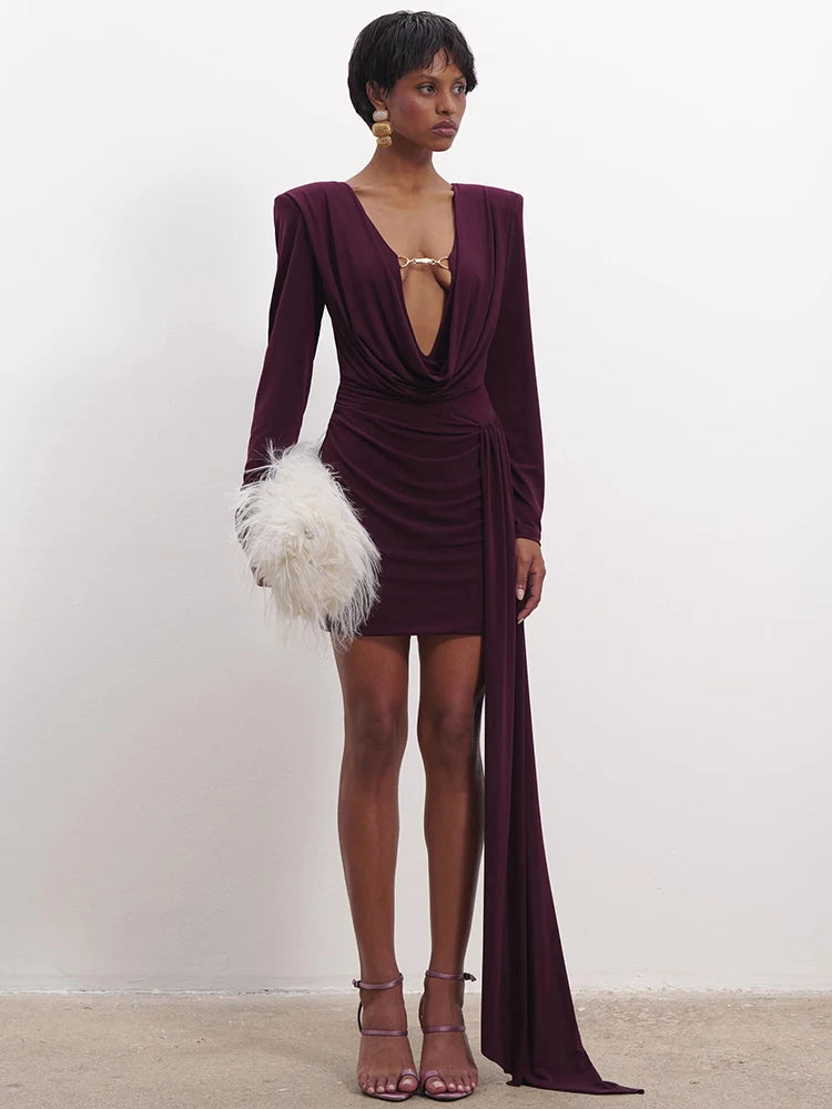 Woman wearing a deep purple dress with a high slit on a plain background