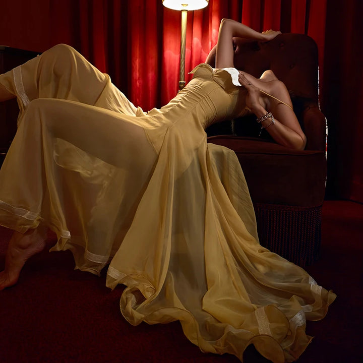 Person in a yellow dress sitting on a red couch with red curtains and a lamp in the background.
