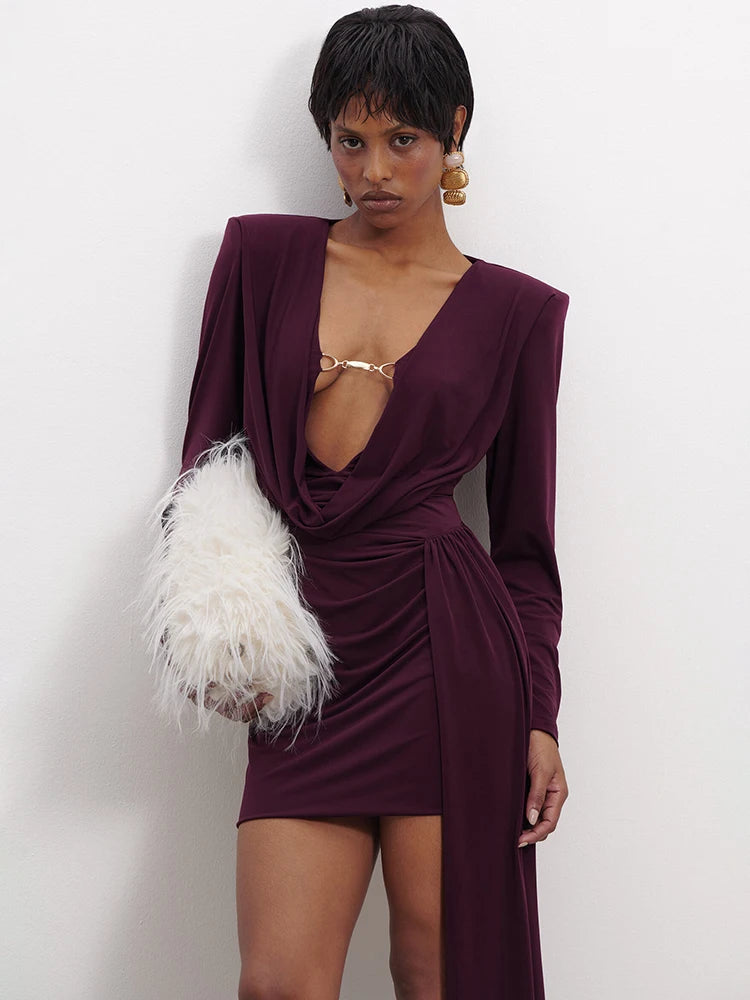 Woman wearing a deep purple dress with a white feathered clutch against a plain background