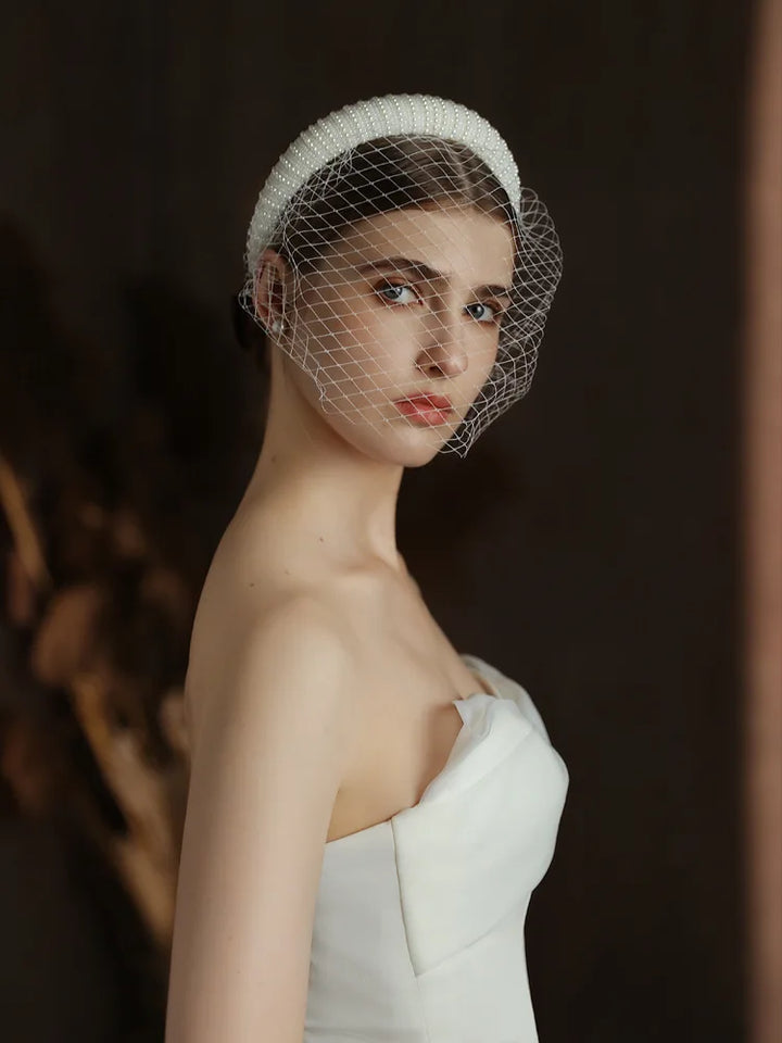 Woman wearing a white strapless dress and birdcage veil against a dark background
