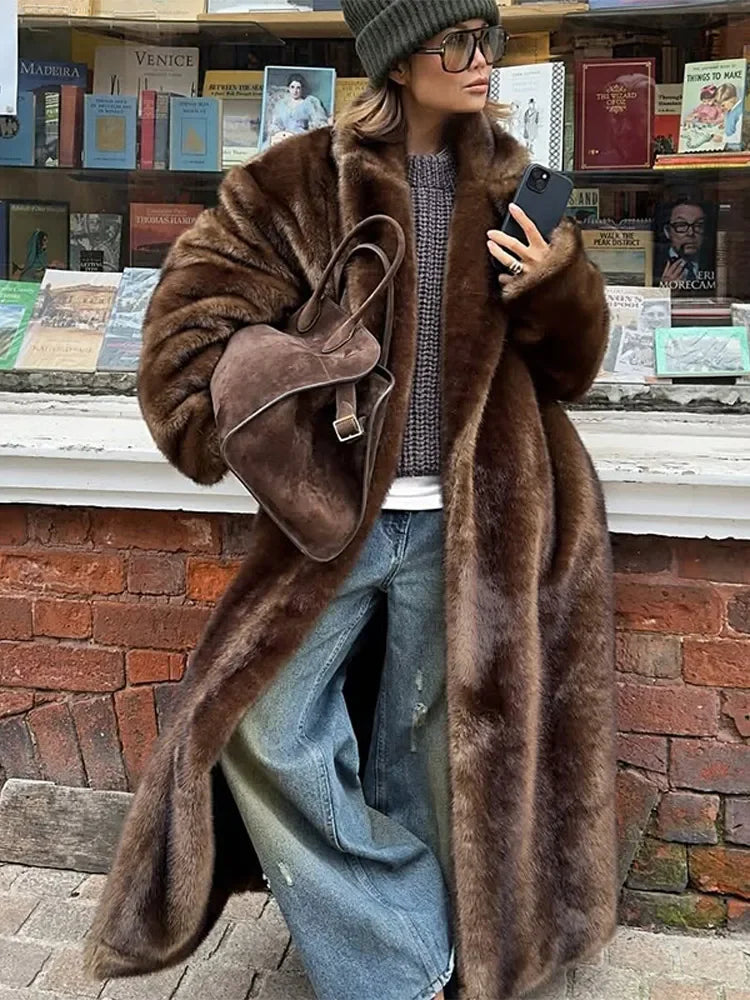 Person wearing a long brown fur coat in front of a bookshelf.
