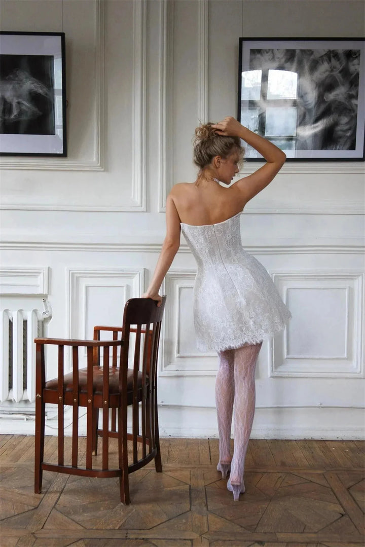 Woman in a white lace dress standing in a room with framed pictures on the wall.