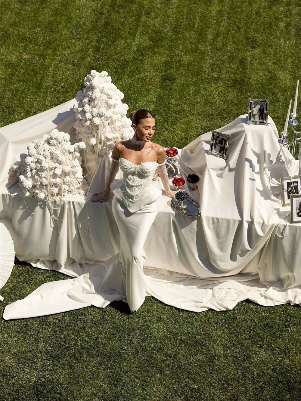 Woman in a white wedding dress standing next to a decorated table outdoors.