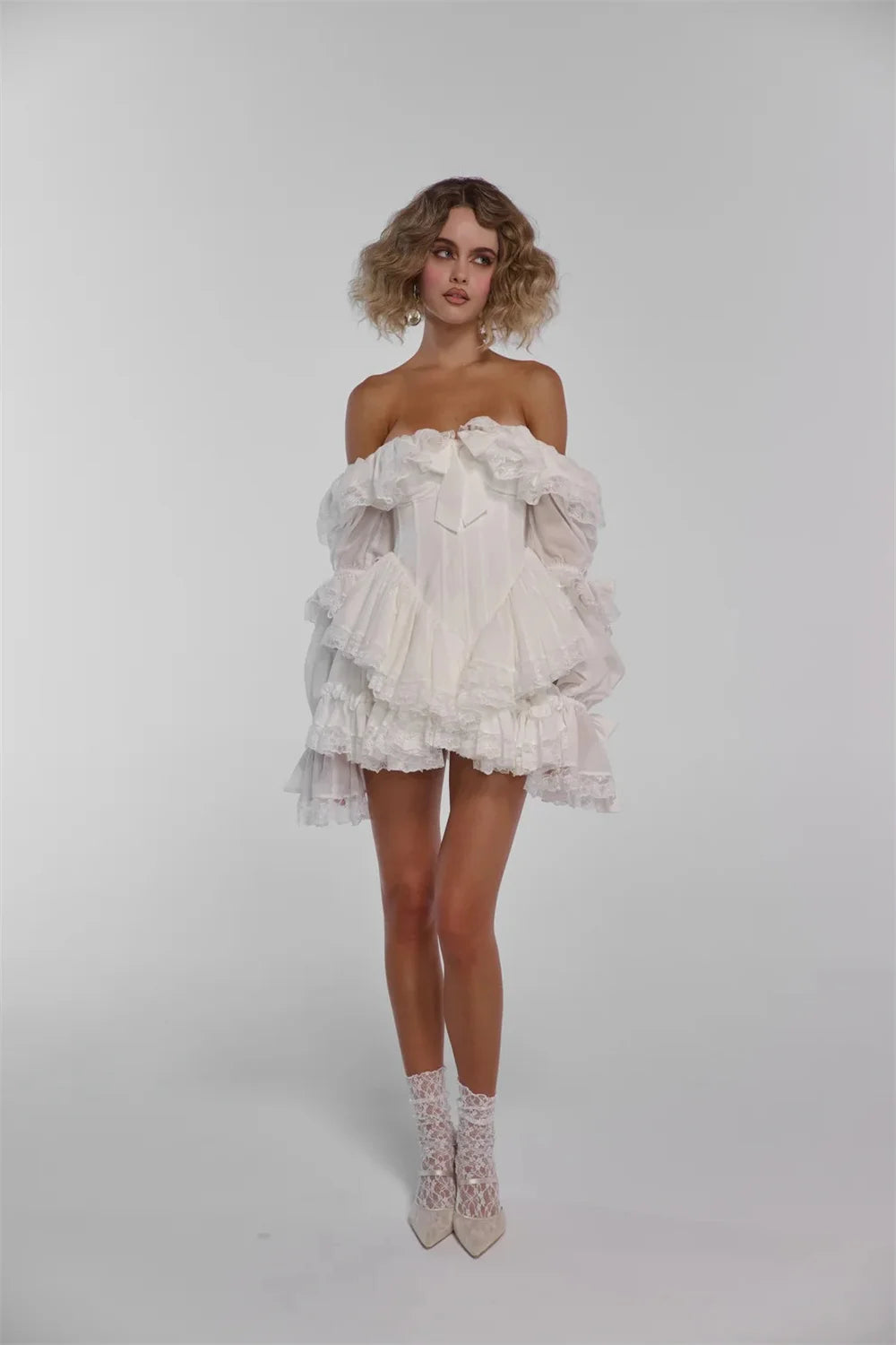 Woman wearing a white ruffled dress and high-heeled shoes on a plain background