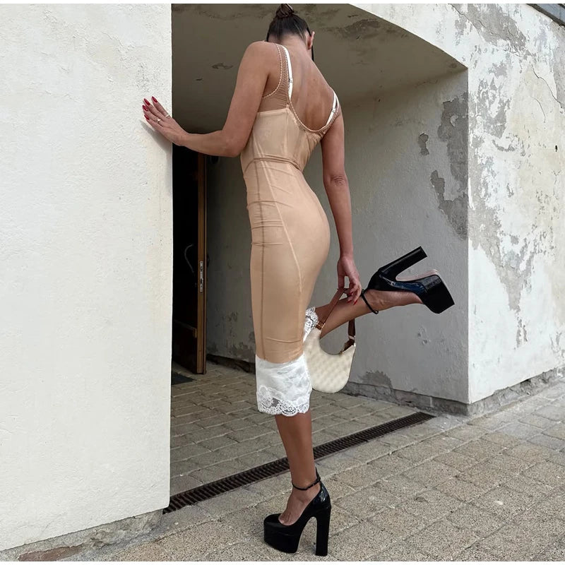 A woman stands in a doorway wearing a fitted nude-beige bodycon dress with thin straps, white lace hem detail, and black high-heeled platform shoes, holding a white handbag.