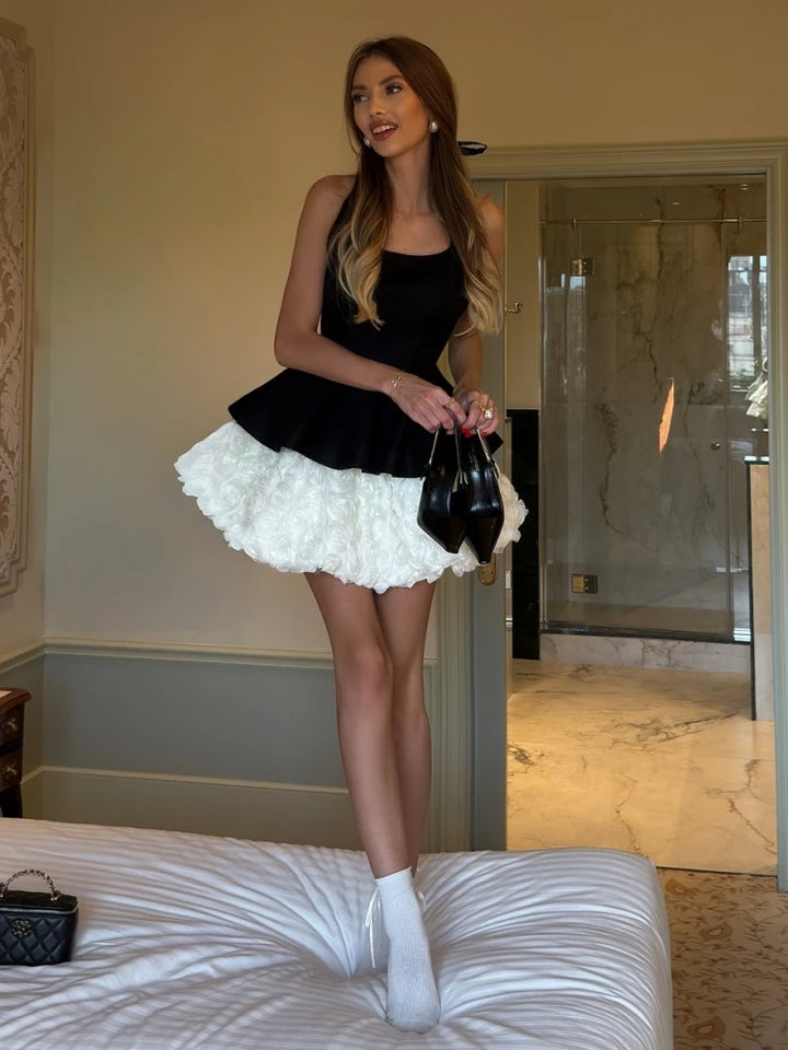 Woman in a black top and white skirt standing on a bed in a room with a mirror.